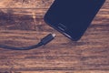 Close-up of black smartphone charging battery with an USB cable on wooden table with copy space Royalty Free Stock Photo