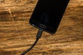 Close-up of black smartphone charging battery with an USB cable on wooden table with copy space Royalty Free Stock Photo