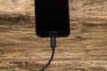 Close-up of black smartphone charging battery with an USB cable on wooden table with copy space Royalty Free Stock Photo