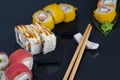 Close-up, on a black table there are assorted Japanese rolls, tuna, with soft cheese and teriyaki sauce and baked rolls in tempura