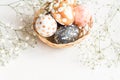 Close up of black, white and golden decorated eeaster eggs in wicker basket decorated with gypsophila on white background