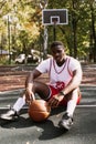 Close-up of a black young man holding a basketball and sitting on a basketball court. Sports concept, healthy movement