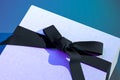 Close up of blank gift box with bow for greetings concept. White gift box with black ribbon bow on blue background. 3d Royalty Free Stock Photo