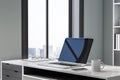 Close up of blank laptop with reflections on office desktop with coffee cup and city view.