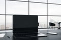 Close up of blank laptop screen on gray office desktop with supplies on panoramic window and city view background. Mock up, 3D