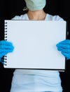 Close-up of blank notebook page held up by woman wearing face mask and surgical gloves with black background Royalty Free Stock Photo