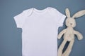 Close up of blank white baby bodysuit grow mockup with cream rabbit soft toy on a light blue background Royalty Free Stock Photo