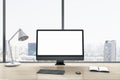 Close up of blank white computer monitor on wooden office desktop with objects, lamp and supplies on panoramic window and city