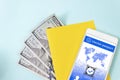 Close up blank yellow piece of paper, 100 dollar bills and digital health passport app in mobile phone on blue background Royalty Free Stock Photo