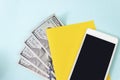 Close up blank yellow piece of paper, 100 dollar bills and empty screen mobile phone on blue background Royalty Free Stock Photo