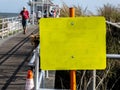 Close-up of a blank yellow sign at the entrance to a wooden pier on a sunny day at the beach