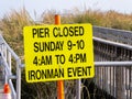 Close-up of a blank yellow sign at the entrance to a wooden pier on a sunny day at the beach near a sand dune with tall grass Royalty Free Stock Photo