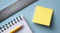 Close-up of blank yellow sticky note, spiral notebook with pencil, and metal ruler on blue surface for or school use Royalty Free Stock Photo
