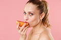 Close up blonde half naked woman 20s perfect skin nude make up blue eyes hold in hand grapefruit isolated on pastel pink Royalty Free Stock Photo