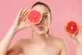 Close up blonde half naked woman 20s perfect skin nude make up blue eyes hold in hand grapefruit  on pastel pink Royalty Free Stock Photo