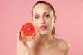 Close up blonde half naked woman 20s perfect skin nude make up blue eyes hold in hand grapefruit  on pastel pink Royalty Free Stock Photo