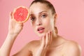 Close up blonde half naked woman 20s perfect skin nude make up blue eyes hold in hand grapefruit  on pastel pink Royalty Free Stock Photo