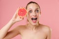 Close up blonde half naked woman 20s perfect skin nude make up blue eyes hold in hand grapefruit  on pastel pink Royalty Free Stock Photo