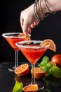 Close-up of blood orange cocktail glasses with woman`s hand with bracelets putting orange slice in a glass, selective focus