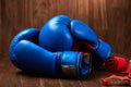 Close-up of the blue boxing gloves and red bandage on wooden background.