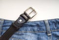 Close-up of blue jeans and a black leather belt on a white isolated background, the concept of men`s casual wear Royalty Free Stock Photo