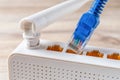 Close-up of blue network cable plug almost inserting into the socket of the white Wi-Fi wireless router on a wooden desk. Home and Royalty Free Stock Photo