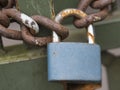 Close up of blue padlock with rusty chain locked at old green gate door, selective focus Royalty Free Stock Photo