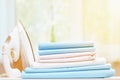 Close-up of blue and white clean bedding on a blurred background. A stack of folded bedsheets on the table, an iron stands nearby. Royalty Free Stock Photo