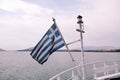 Close up of blue and white Greek flag on flagpole flying in wind. Torn Greek national flag waving on bow of ship against blue sea. Royalty Free Stock Photo