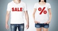 Close up of the bodies of man and woman in a white t-shirts with the red percentage sign and the word ' sale ' on the chest.