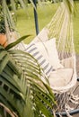 Close-up of a boho hammock hanging in a sunny garden with a palm