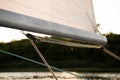 Close up on the boom mast of a sailing yacht, with sail and rigging ropes, and river or lake coast in the background