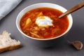 Close up borscht with sour cream in a bowl with bread on a gray table