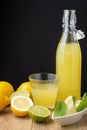 Close-up of bottle with lemonade, glass, lemon wedges, lime, mint and whole lemons, on wooden table and black background, vertical Royalty Free Stock Photo