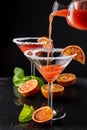 Close-up of bottle pouring blood orange martini, two glass goblets, with selective focus, with half orange and mint, on black back Royalty Free Stock Photo