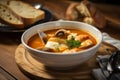 Close-up of Bouillabaisse soup served in a white ceramic bowl with a spoon and a side of crusty bread on a rustic wooden table