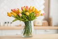 Close-up of a bouquet of fresh spring yellow tulips in a large transparent glass vase in a photo studio against the background of