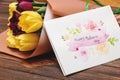 Close up of bouquet of fresh tulips with craft postcard on wooden background. Royalty Free Stock Photo