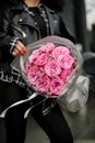 Close-up of a bouquet of pink roses with tiny daisies, wrapped in gray wrapping paper, which female hands carefully