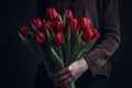 Close-up of a bouquet of red tulips in the hands of a girl in a blouse on a dark background