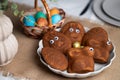 Close-up of funny muffins shaped as bunnies and eggs with eyes, multi colored Easter eggs in wicker basket on served