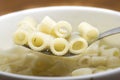 Close up of a bowl of macaroni soup. Spoon picking up macaroni,