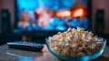 Close up of bowl of popcorn and remote control with tv works on background. Evening cozy watching a movie or TV series