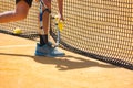 Close-up of a boy with a tennis racquet picking up yellow balls by the net on a clay court Royalty Free Stock Photo