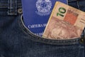 Close up of brazilian banknotes and Brazillian Work Card in a pocket. Formal employment concept. Translate: Work and social