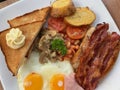 close up breakfast plate include fried eggs, ham, sausages, potatoes, tomatoes, mushrooms, beans