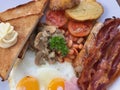 close up breakfast plate include fried eggs, ham, sausages, potatoes, tomatoes, mushrooms, beans