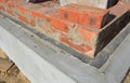 A close-up of bricklaying a house wall corner with the first course of bricks laid over a concrete foundation, basement with a