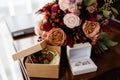 Close up of bridal bouquet of pink, orange and red flowers, butonniere and two golden wedding rings in box on table indoors. Royalty Free Stock Photo