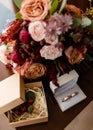 Close up of bridal bouquet of pink, orange and red flowers, butonniere and two golden wedding rings in box on table indoors. Royalty Free Stock Photo